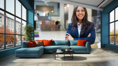 Happy successful businesswoman posing in office hall. Young Latin woman wearing formal suit and glasses, standing for camera with arms folded, smiling. Business portrait concept Wall mural