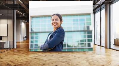 Happy successful young businesswoman posing outside. Beautiful Latin woman wearing formal jacket, standing near office building, looking at camera and smiling. Successful career concept Wall mural