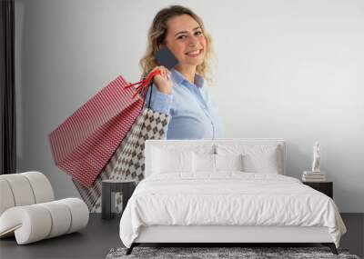 Happy woman enjoying shopping and paying with credit card. Smiling excited young lady in blue blouse carrying shopping bags on back and looking at camera. Cashless payment concept Wall mural