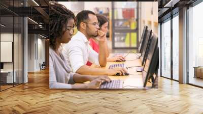 Multiracial group of students training in computer class. Line of man and women in casual sitting at table, using desktops, typing, looking at monitor. Training center concept Wall mural