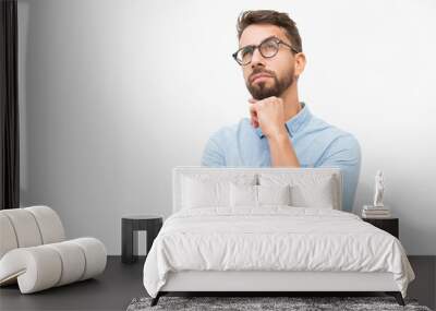 Pensive customer thinking over special offer, touching chin, looking up. Handsome young man in casual shirt and glasses standing isolated over white background. Advertising concept Wall mural