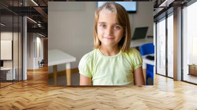 Portrait of blonde pretty girl in yellow shirt. Lovely Caucasian kid posing in classroom after lesson, smiling and looking at camera. Front view. Selective focus. People, study and appearance concept Wall mural