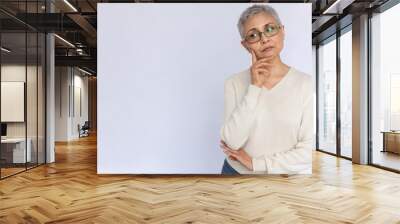 Portrait of thoughtful senior woman wearing eyeglasses and white jumper. Mature Caucasian woman standing with hand on chin and thinking over white background. Planning concept Wall mural