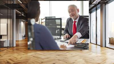 Positive boss with asking face pointing at mistakes in notes of employee. Mature grey haired man in formal jacket instructing young worker in modern office space. Mentorship and leadership concept Wall mural