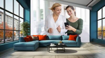 Positive female office employees posting selfies on internet. Two women in office clothes walking outdoors and using phone. Mobile connection concept Wall mural