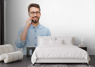 Positive guy talking on cellphone, enjoying nice conversation. Handsome young man in casual shirt and glasses standing isolated over white background. Phone call concept Wall mural