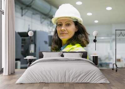 Positive successful female engineer posing on plant floor. Middle aged woman in uniform and hardhat looking at camera. Industrial job concept Wall mural