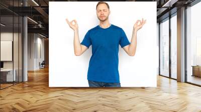 Relaxed man standing and showing zen gesture. Peaceful man standing in lotus position on white background, meditating with closed eyes and breathing. Yoga, relaxation concept Wall mural