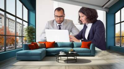 Serious coworkers using laptop. Professional multiethnic businessman and businesswoman sitting at table and working with laptop computer in office. Business and technology concept Wall mural