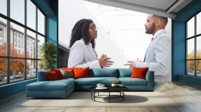 Serious excited business partners arguing about deal in office hall. Business man and woman standing in hallway, talking and gesturing. Negotiation concept Wall mural