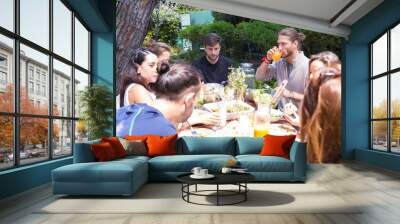 Serious male and female friends having dinner outdoors. Young women and men eating salads and drinking juice in garden. Outdoor party concept Wall mural