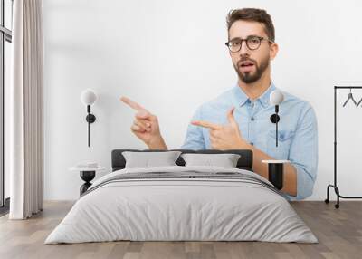 Serious surprised male customer presenting copy space, pointing fingers away. Handsome young man in casual shirt and glasses standing isolated over white background. Advertising concept Wall mural