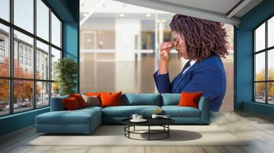 Serious upset female employee thinking over bad news outside office. Young African American business woman standing at glass wall with head low, touching face, looking into vacancy. Bad news concept Wall mural