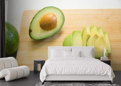 Sliced avocado and halved fruit with seed on chopping board. Top view. Isolated objects on white background. Fresh food or healthy diet concept Wall mural