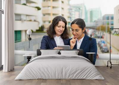 Smiling businesswomen using tablet pc. Cheerful focused female colleagues standing with digital tablet on urban city street. Wireless technology concept Wall mural