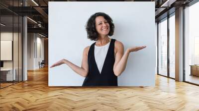 Smiling woman gesturing with hands. Attractive middle aged brunette woman with curly hair gesturing with hand and smiling at camera. Gesture concept Wall mural