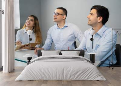 Three smiling young business colleagues sitting at meeting in office. Businesspeople listening to coach at seminar. Meeting or business training concept Wall mural