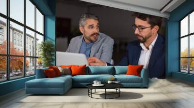 Two tired businessmen talking in dark office. Two office managers sitting at table with laptop and communicating. Business, working late concept Wall mural