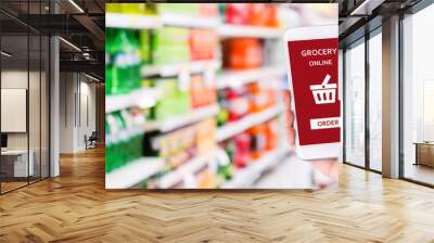 Hand holding smartphone with grocery online shopping application on device screen over blur supermarket background, business and technology, lifestyle concept Wall mural