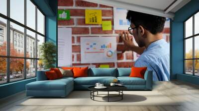 Young asian creative design man reading and thinking about paper work ideas on office wall with concentration, Working  asian man reading brainstroming ideas at office, Creative occupation lifestyle Wall mural