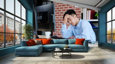 Young asian man with frustrated expression while working with computer at office desk, office lifestyle Wall mural