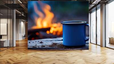 A steaming cup of hot coffee, blue enamel against an old log by an outdoor campfire. The camera captures an extreme shallow depth of field with the mug in sharp focus. Wall mural