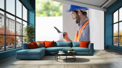 A portrait of an industrial man engineer with smartphone in a factory, working. Wall mural