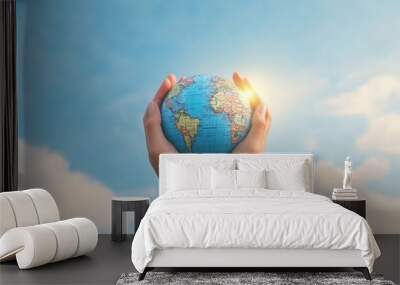 A pair of hands gently holding a miniature globe against a bright sky, symbolizing care and responsibility for our planet. Wall mural