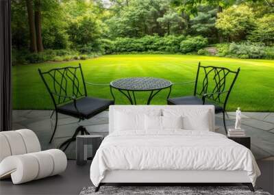 Cozy outdoor seating area with two black chairs and a small table surrounded by lush greenery and a tranquil lawn. Wall mural