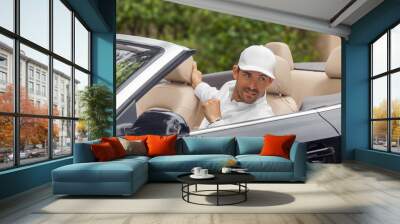 A man setting in a convertible car looks over at something or someone out of frame. A businessman wears a business casual white baseball cap and a white long-sleeve button-down shirt. Wall mural