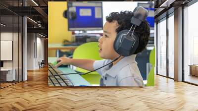 a small boy wearing oversized headphones navigates a wireless mouse in front of the computer. he rem Wall mural