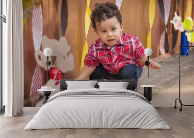 Toddler squats down to pick up an object at a party looking at the camera. Wall mural