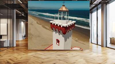 Torre de un faro de color blanco y rojo a orillas de una playa en la serena chile. De fondo se ve la playa, las olas del mar y la ciudad de Coquimbo Wall mural