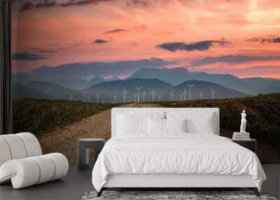 large onshore wind farm in the atmospheric evening light in front of mist-covered mountains, in the foreground leads a dirt road to the wind turbines Wall mural