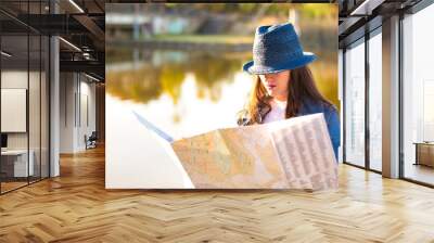 Young woman with blue hat and denim jacket consulting a map during a trip. Wall mural