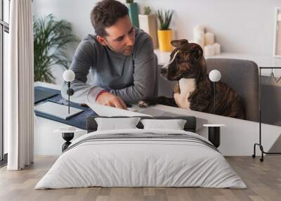 Freelancer man working from home with his dog sitting together in the office Wall mural