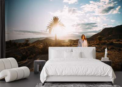 Portrait of an attractive young woman posing smiling in a wonderful desert landscape with a palm tree and mountains in the background.  Advertising photography. Fashion and lifestyle concept Wall mural