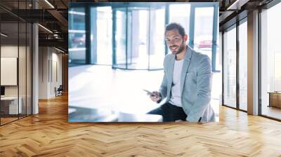 smiling young businessman sitting on a sofa talking to the smartphone in his office. business concept Wall mural