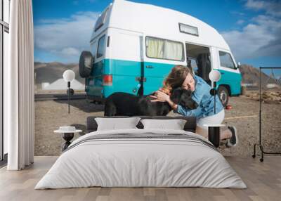 young woman hugging her dog in front of a blue classic van in the beach Wall mural