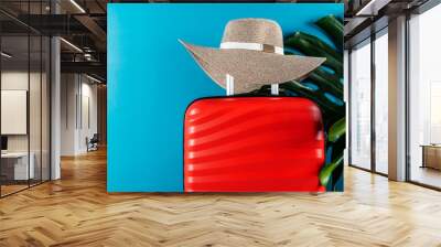 Bright and stylish cabin size suitcase with straw hat and monstera leaf against dark blue background. Easy travel with little baggage concept. Copy space. Wall mural