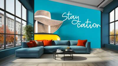 staycation word. bright and stylish cabin size suitcase with straw hat against bright blue backgroun Wall mural