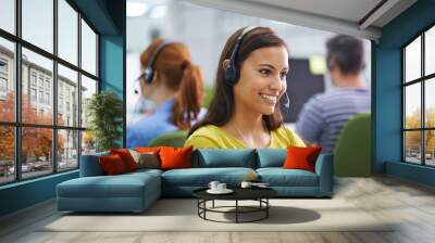 How can I help you. Shot of an attractive female at work wearing headsets. Wall mural