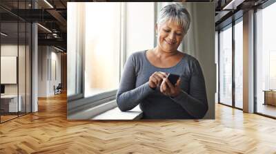 Window, smile and senior woman with a smartphone, connection and social media at home. Mature female, person and old lady with a cellphone, email and mobile app with network, happiness and typing Wall mural