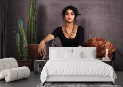 Ethnically at ease. Studio portrait of a beautiful young woman sitting amongst cacti and cushions. Wall mural