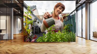 Happy caucasian woman watering the plants and aromatic herbs at the garden in her balcony on a cloudy day Wall mural