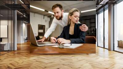 A bearded male Manager harasses his colleague a girl who works at a laptop in the office Wall mural