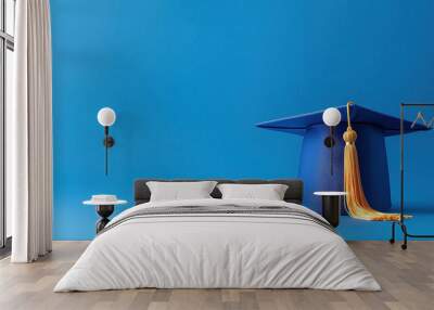 A blue graduation cap with a golden tassel set against a solid blue background, symbolizing academic achievement, perseverance, and the celebration of educational milestones. Wall mural