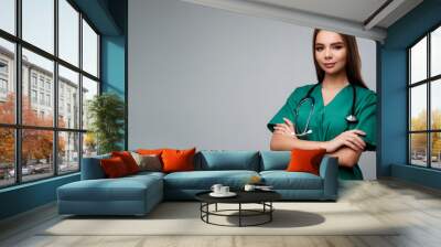 A woman in a green scrubs shirt is smiling and holding her arms crossed Wall mural