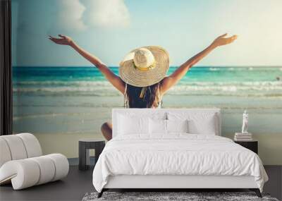 summer vacation happy carefree joyful bikini woman arms outstretched in happiness enjoying tropical beach destination holiday girl sitting with sun hat relaxing from behind on caribbean vacation Wall mural