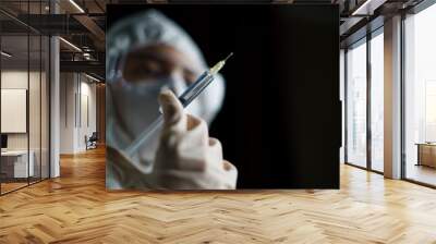 Woman wearing gloves with biohazard protective suit and mask holds an .virus vaccine with syringe, for prevention and treatment from corona virus (Covid-19) Wall mural